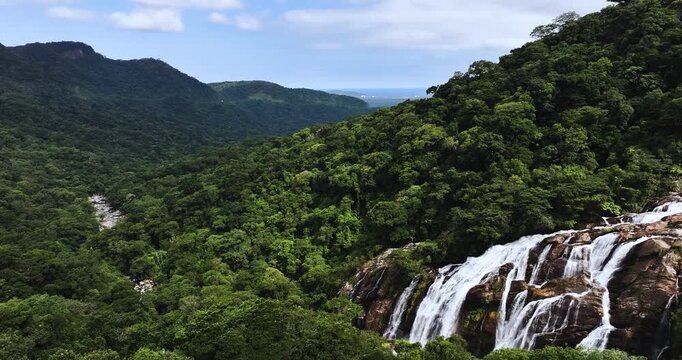 Cinematic aerial 4K footage of Veu da Noiva waterfall located in the Serra do Mar, Brazil. The scene showcases powerful cascading water flowing over rocky cliffs surrounded by dense tropical rainfores