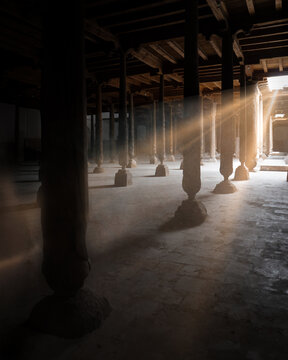 View of the historic Juma Mosque interior featuring intricately carved wooden columns and sunbeams streaming through the ceiling, Khiva, Xorazm Region, Uzbekistan.