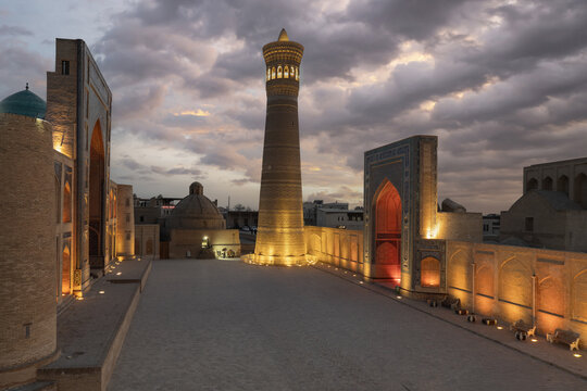 View of the illuminated Kalyan Minaret and Po-i-Kalyan complex at dusk under a cloudy sky in Bukhara, Bukhara Region, Uzbekistan.