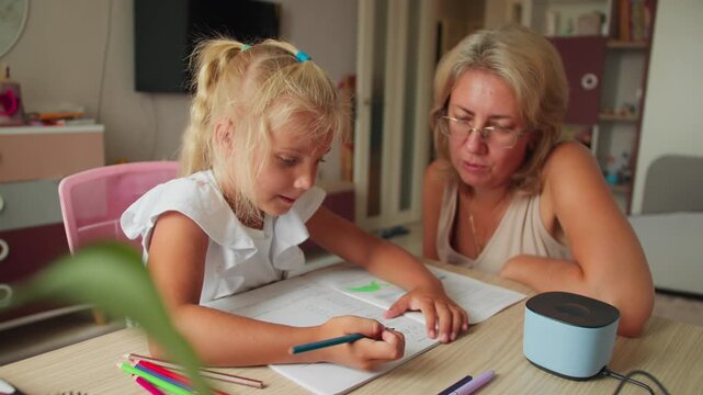 Mother explaining homework to her daughter at home desk. Learning with parental guidance concept