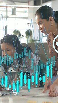 Vertical video: Two women working in biz, right pointing causing charts over laptop reviewing docs