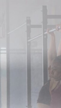 Vertical video: Women reaching for bar, initiating pull-up reps while spotter supporting in fitness