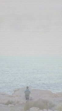 Vertical video: Woman walking toward sea on rocky shore seeking view sparking animated fog for film