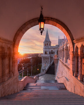 View of the Fisherman's Bastion through a stone archway with stairs and a glowing sunset sky in Budapest, Hungary.