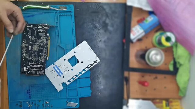 Top-down view of a disassembled high-end graphics card (GPU) on a blue magnetic repair mat for cleaning and thermal paste replacement.