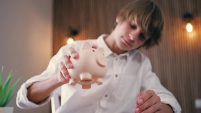 Teen boy shaking piggy bank to get coins, counting savings and planning budget, financial literacy, money management and personal finance concept at home.