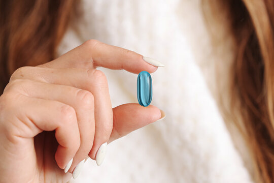 Blue softgel capsule held between fingers in macro closeup. Supplement background with healthcare concept. Personal vitamin detail. Wellness dosage scene.
