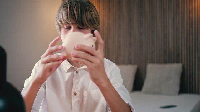 Young teen boy excitedly shaking piggy bank, checking savings and dreaming of financial freedom, portraying early economic education and personal finance management at home
