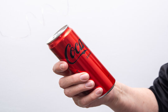Coca-Cola in hand thin aluminum can zero sugar 330 ml no calories. Red slim classic can. Black label logo front view. Gray background. Ukraine, Kyiv - April 21, 2025.