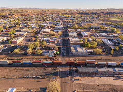 Holbrook, United States - 05 April 2026: Aerial view of the town of Holbrook with a long freight train crossing the main road, surrounded by low-rise buildings and a desert landscape at sunset.
