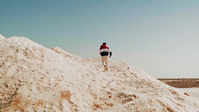a traveler young man wearing a jacket walking alone on the mountain of salt near salt lakes in siwa oasis in egypt