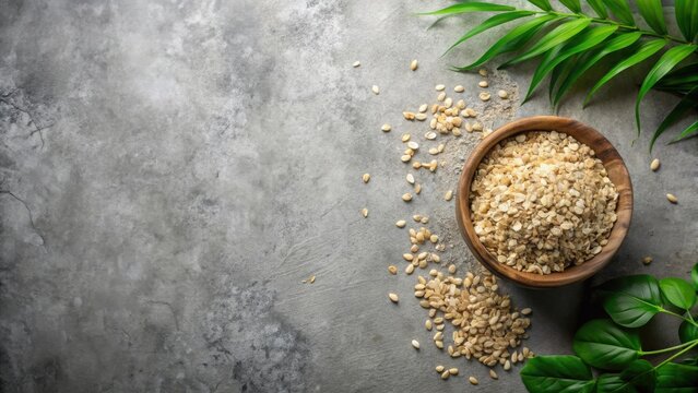 Wooden bowl filled with nutritious oat flakes and scattered grains, complemented by vibrant green foliage on a textured gray surface