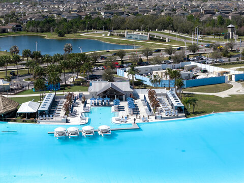 Wesley Chapel, United States - 02 March 2026: Aerial view of Epperson Lagoon featuring turquoise water, white cabanas, and lounge chairs surrounded by palm trees and suburban houses.