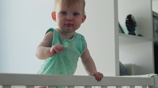 Baby girl standing in crib and practicing upright position. Baby milestones first steps