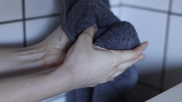 A woman&rsquo;s hands are dried with a towel after washing at a sink indoors. The action shows a basic hygiene routine of drying hands.