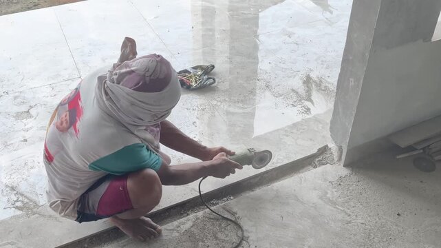 Construction worker grinding and smoothing granite floor tile edges with a hand angle grinder. Precision granite edge finishing work.