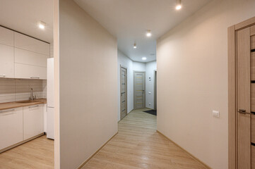 Fototapeta premium modern hallway with light wooden flooring, beige walls, recessed ceiling lights, three wooden doors with glass inserts, adjacent to a white kitchen with wooden countertops