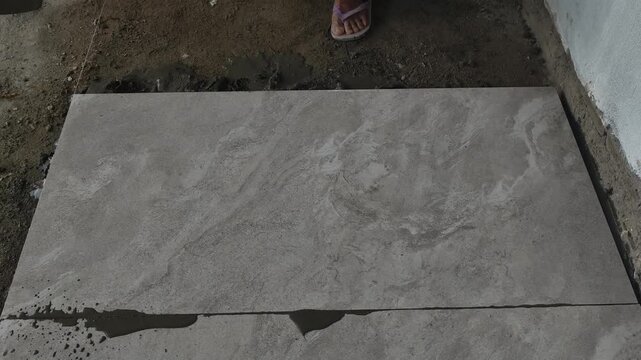 Construction worker tapping granite floor tile with a rubber mallet to level the surface during floor installation. Precision tiling work.