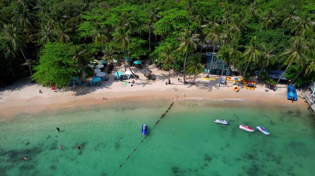 Stunning aerial footage of Hon Vong Island Beach with turquoise blue water and sandy beach with tourist boats anchored and people swimming on a hot summer day in Phu Quoc South Vietnam