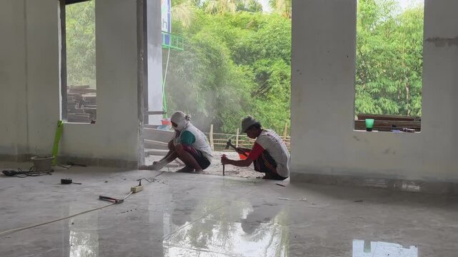 Two construction workers fixing a bottom wall base &mdash; one with an angle grinder, the other using a chisel and hammer. Collaborative work.