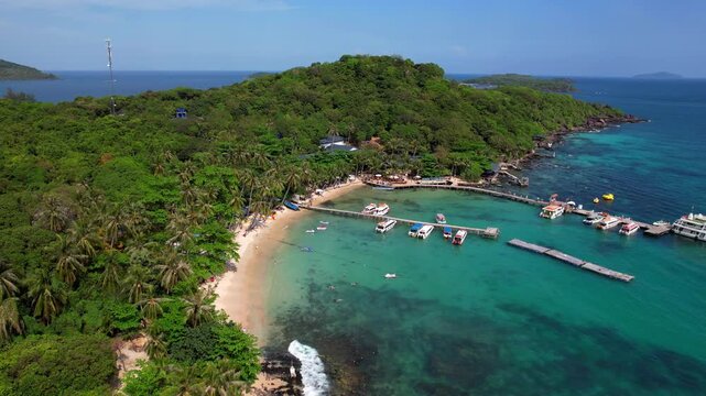 Stunning aerial footage of Hon Vong Island Beach with turquoise blue water and sandy beach with tourist boats anchored and people swimming on a hot summer day in Phu Quoc South Vietnam