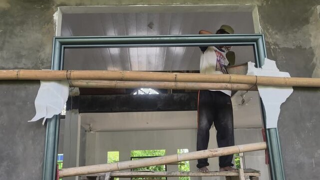 Construction worker pouring wet cement mixture into the inside of a door frame for structural reinforcement during construction.