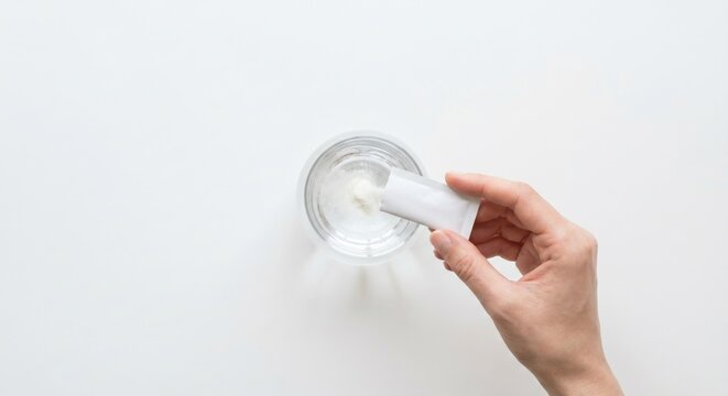 Hand pouring collagen powder sachet into glass of water