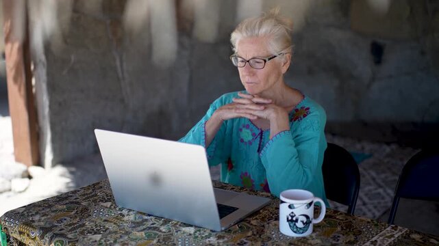 Mature woman types on a computer while sitting under a palapa on a tropical beach in Baja California Mexico enjoying her work abroad.