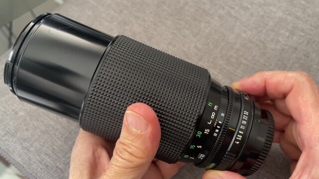 a hand rotating the zoom ring on a black manual vintage camera lens showcasing detailed markings for focal length distance and aperture settings for professional photography and videography equipment