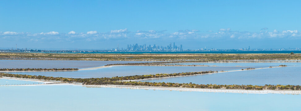 Aerial panorama view of coastal salt ponds under blue sky and distant city skyline