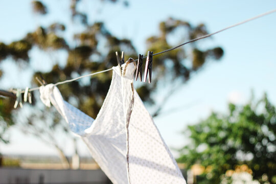White patterned fabric clipped into the clothesline with wooden clothespins under the sunlight