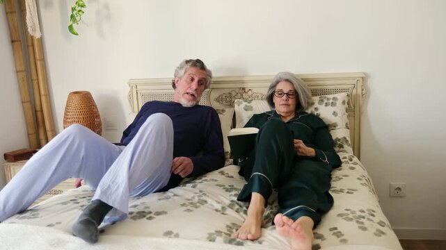 Mature husband and wife in their pajamas spending a relaxing evening reading together in bed