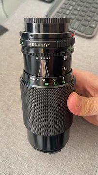 a hand rotating the zoom ring on a black manual vintage camera lens showcasing detailed markings for focal length distance and aperture settings for professional photography and videography equipment