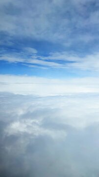 Beautiful white fluffy clouds seen from airplane window during flight high in blue sky above thick atmospheric mist layers on vertical screen.