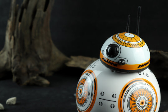 a droid robot character in the Star Wars movie name BB-8 (or Beebee-Ate) display on black stone table with background of black space wall and wood trunk in the star war movie toy shop robot toy
