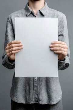 Person holding blank white paper sheet for presentation or announcement against a gray background