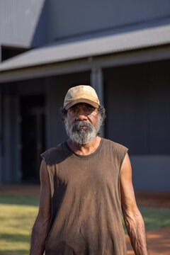 upper body of Aboriginal man with greying beard standing outside wearing a cap and singlet