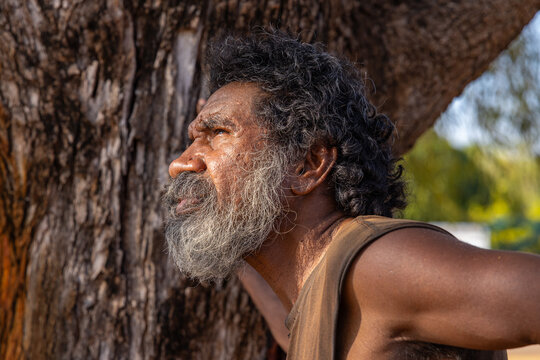 head and shoulders of first nations australian man in profile against the bark of a tree trunk