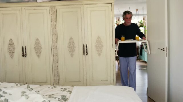 Loving elderly husband bringing a surprise breakfast tray with juice and pancakes to his wife