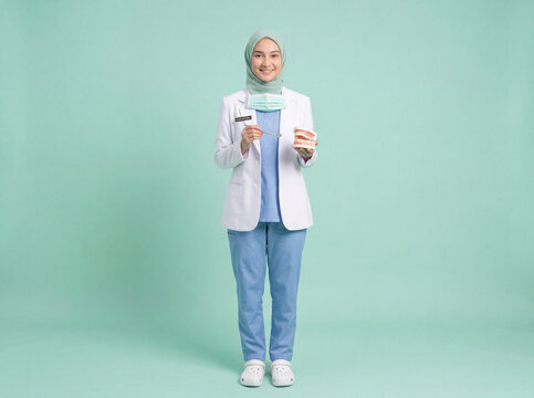 Smiling Muslim Woman Dentist in Mint Hijab Holding Dental Mirror and Teeth Model on Mint Green Background