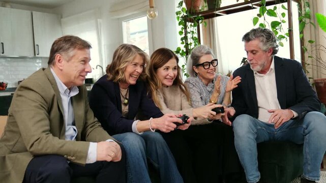 Group of excited senior friends winning a video game and celebrating together on a living room sofa