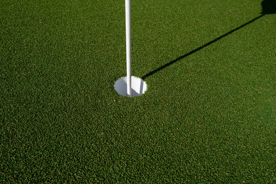 Close-up detail of a golf hole with flagstick on an artificial turf putting green.