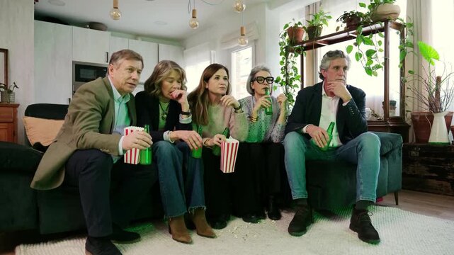 Senior friends watching a sports match together on a sofa, looking upset after a loss