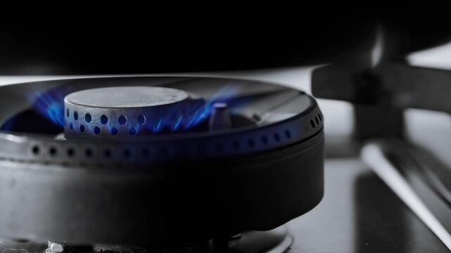 Macro close up of kitchen gas stove burner igniting with bright blue flames, domestic natural gas energy heating power cooking appliance detail