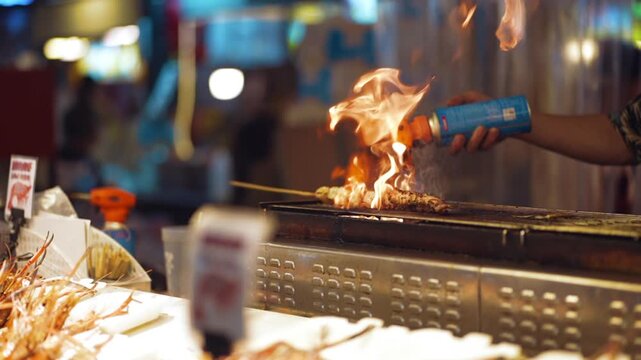 Street food vendor grilling octopus with flame torch at night market, Seafood cooking on grill in Bangkok street market with fire and fresh meal 4k