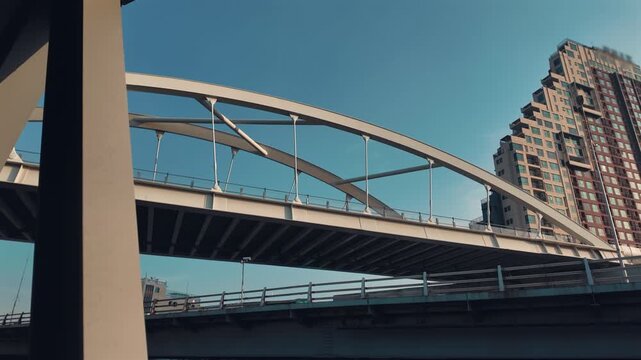 Modern urban bridge overpass with steel arch structure and city buildings in Bangkok, Elevated highway bridge with architectural lines and highrise skyline under blue sky 4k