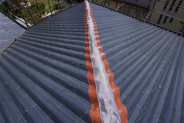 Fototapeta premium Installation of a roof ridge ventilation and sealing system. A roofer installs a ridge cap on a metal roof. Roofing work. Sandwich panels in the form of tiles.