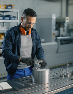 A man in a factory works on a metal cylinder with safety gear.