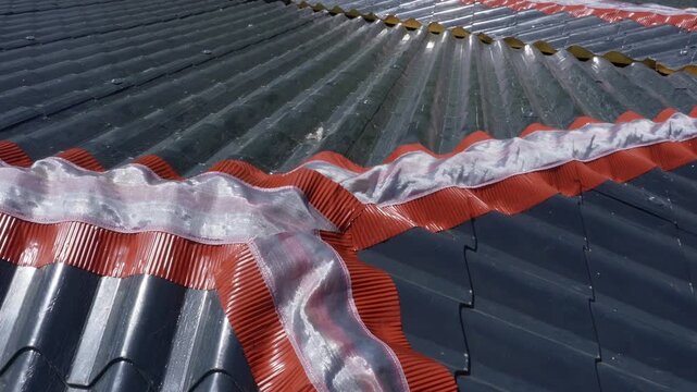Installation of a roof ridge ventilation and sealing system. A roofer installs a ridge cap on a metal roof. Roofing work. Sandwich panels in the form of tiles.