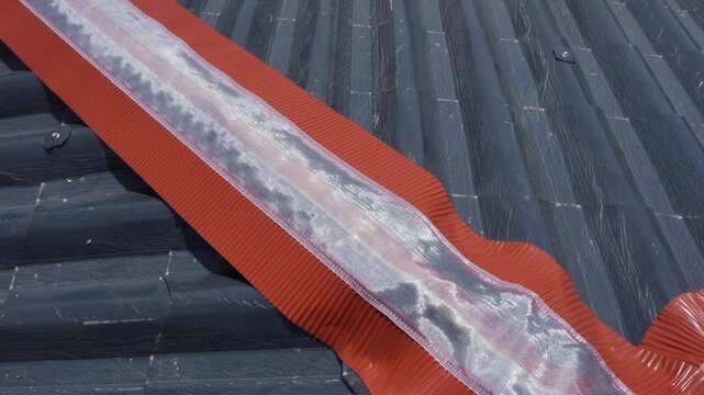 Installation of a roof ridge ventilation and sealing system. A roofer installs a ridge cap on a metal roof. Roofing work. Sandwich panels in the form of tiles.